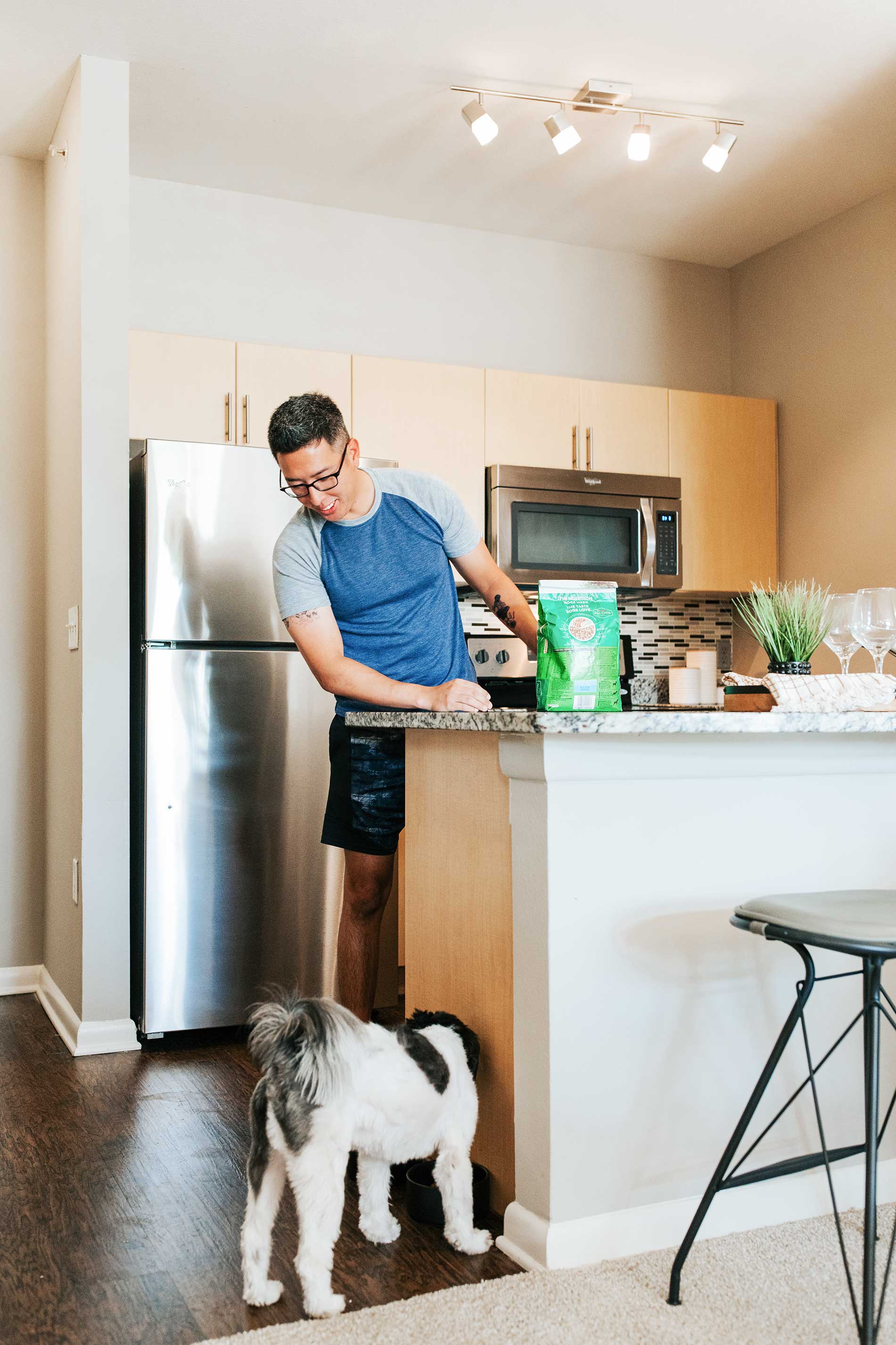 Legacy VIllage man feeds small black and white dog in apartment kitchen
