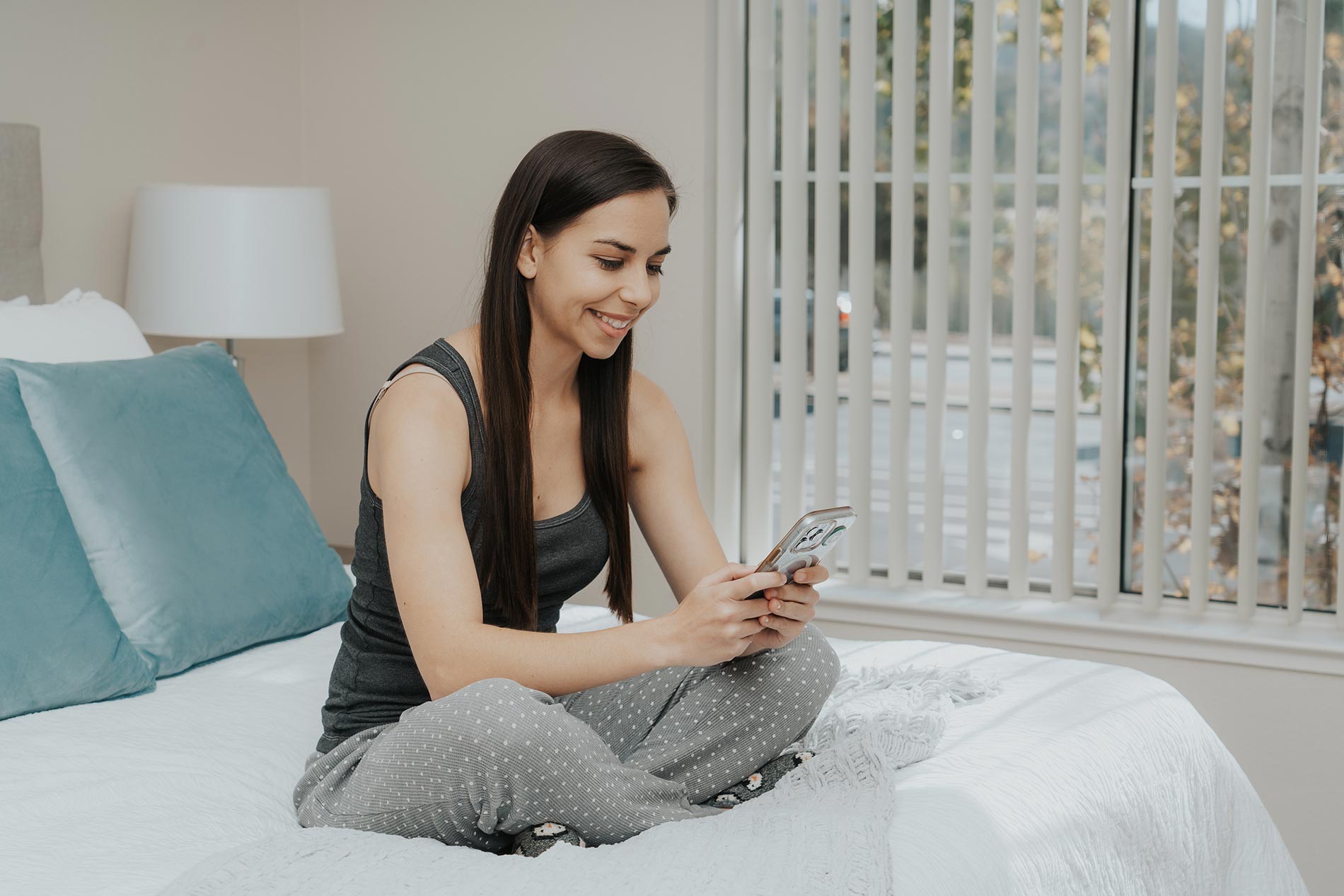 Woman sits on a bed with her phone