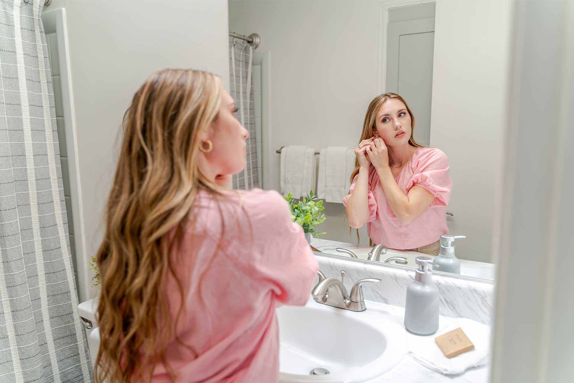 Woman fixing earring in bathroom mirror